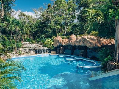 Una piscina tropical de hotel con agua azul clara, rodeada de vegetación exuberante y rocas
