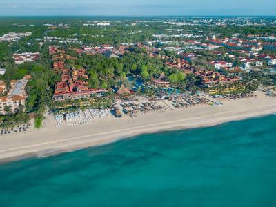 Vista aérea de un resort frente al mar con playa extensa y área de sombra con palmeras.
