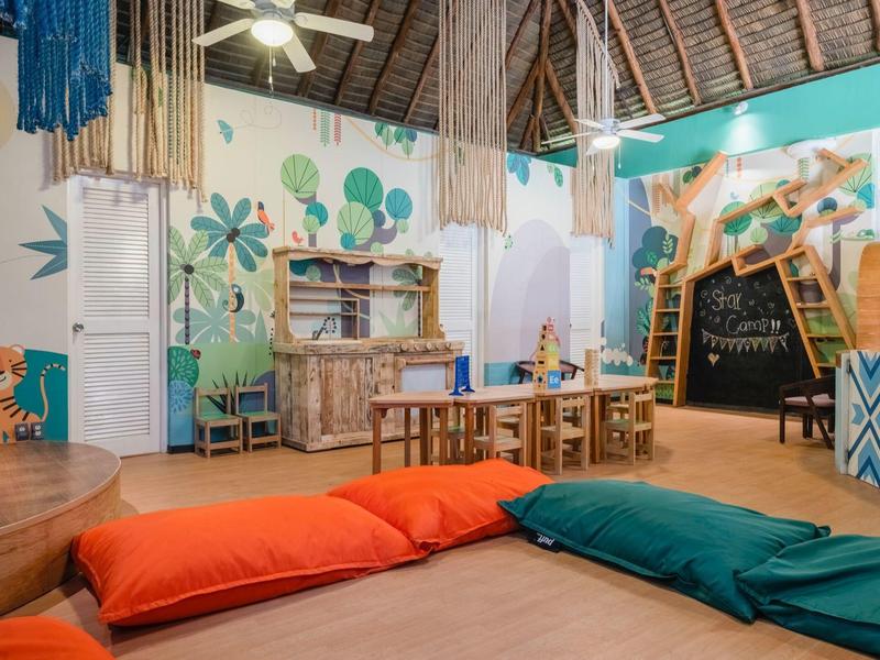 Colorida y acogedora zona infantil con cojines, mesas y decoración creativa en ambiente hotelero.