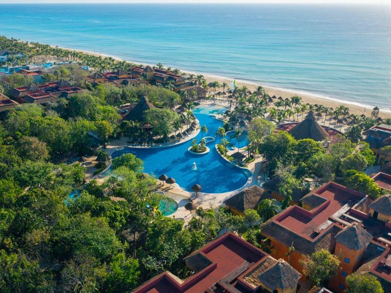 Resort con varias piscinas junto a la playa, rodeado de mucha vegetación y edificios.