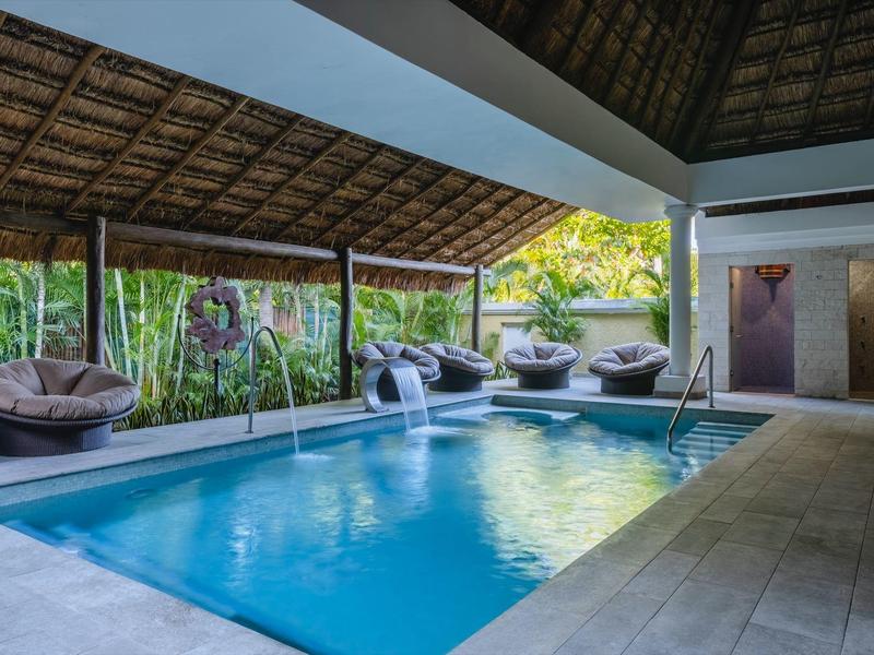 Piscina cubierta con techo de paja y sillas colgantes en un entorno tropical de hotel.