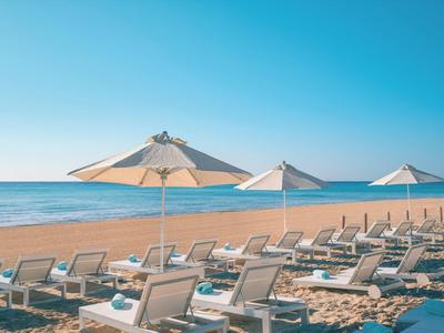 Strand mit Sand, mehreren Liegestühlen und großen weißen Sonnenschirmen unter klarem Himmel.