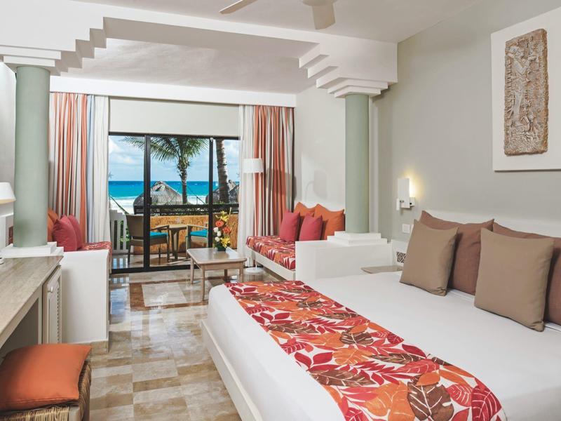 Bright hotel room with sea view, balcony, and cozy seating area.