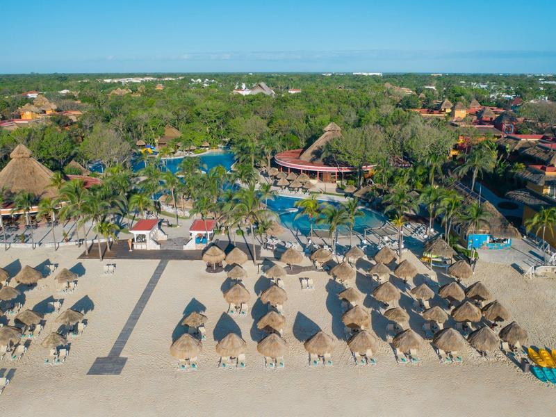 Beach with straw parasols, sun loungers, and tropical greenery in the background.