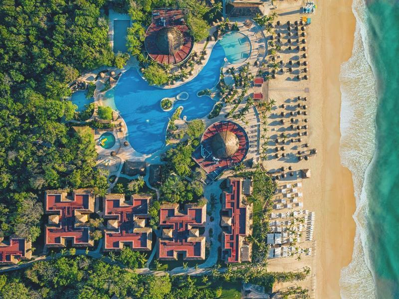 Aerial view of a resort with pool, bungalows, beach, and surrounding forest.
