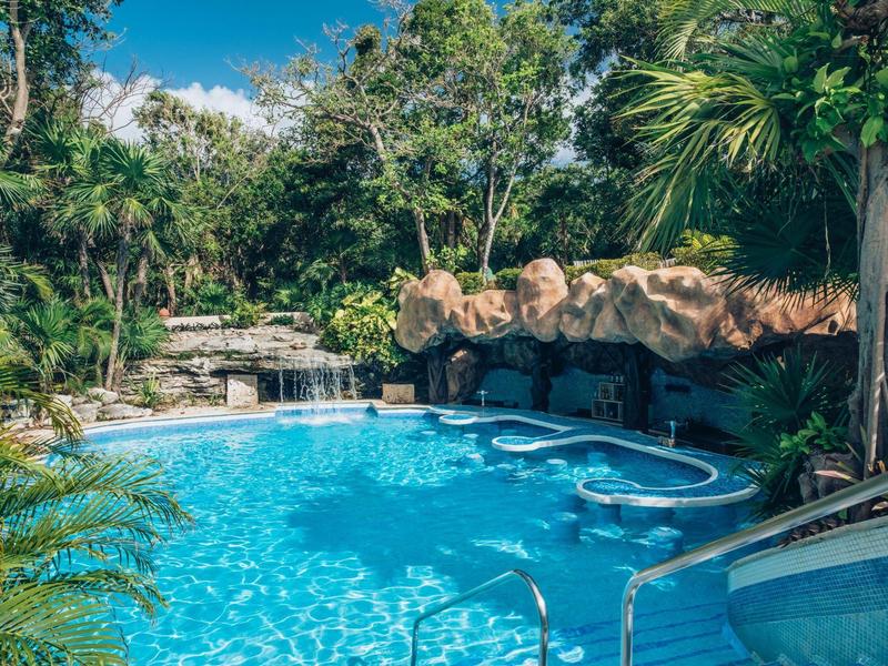 A tropical pool with clear water, surrounded by lush greenery and rocks.