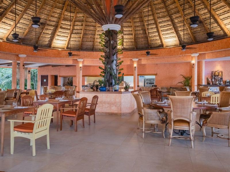 Large open dining area with thatched roof, wooden furniture, and central plant decoration.