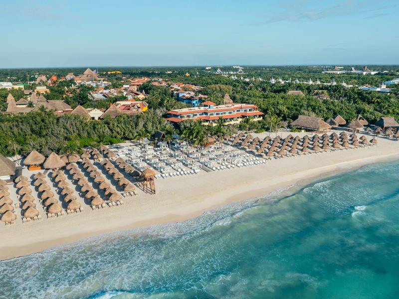 Spiaggia con file di ombrelloni e amache davanti a un hotel in un ambiente tropicale.
