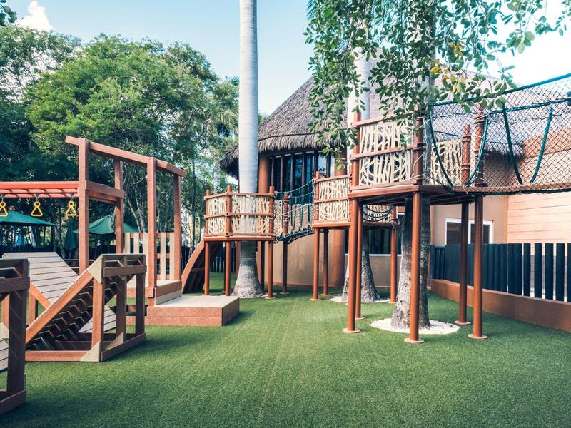 Area giochi esterna moderna con struttura da arrampicata e prato artificiale in un giardino d'hotel.