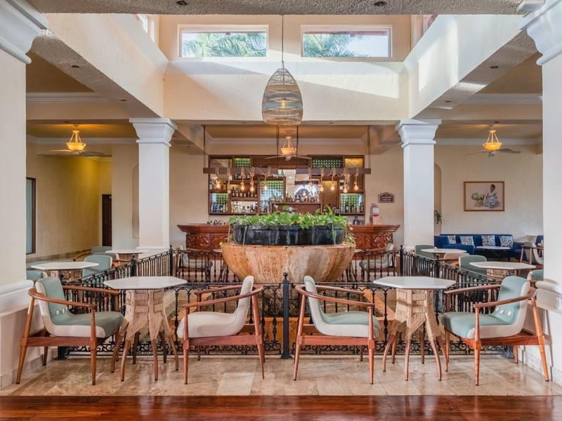 Ristorante d'hotel luminoso e moderno con mobili in legno e bar centrale sotto grandi finestre.