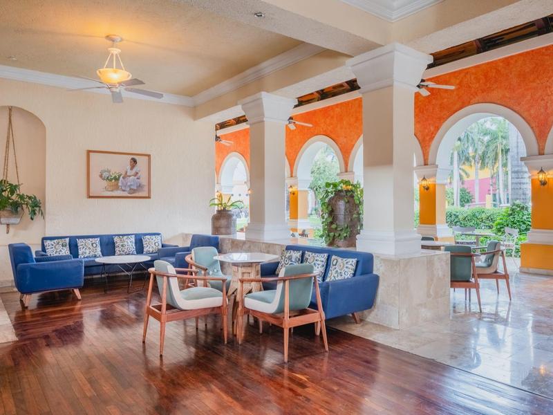 Elegante area lounge dell'hotel con divani blu, sedie e grandi finestre con vista sul verde.