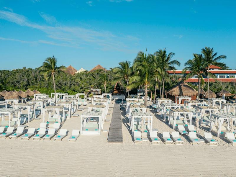 Spiaggia con molte sdraio e palme davanti a un hotel sotto un cielo limpido.