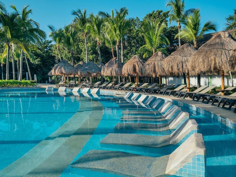 Piscina con lettini e tetti di paglia davanti a palme in un resort tropicale
