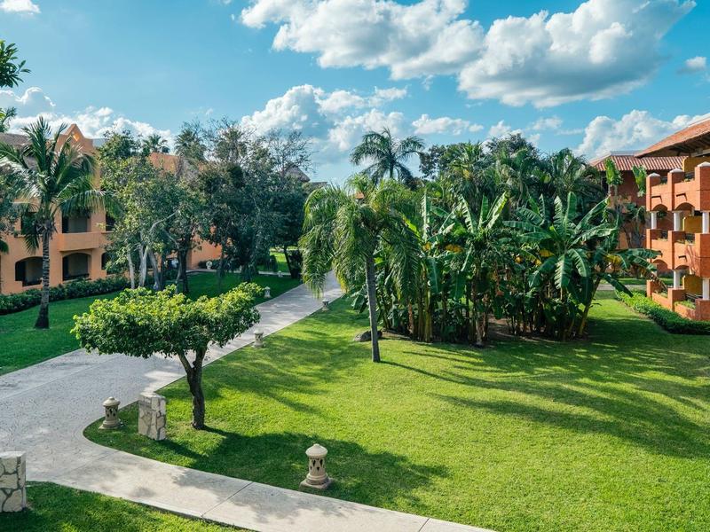 Giardino verde dell'hotel con palme, banani e edifici sotto un cielo azzurro.