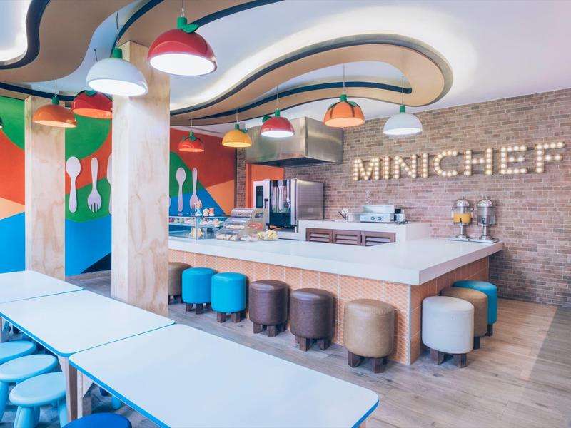 Area pranzo moderna con sgabelli colorati e tavoli in un ristorante d'hotel chiamato MINICHET