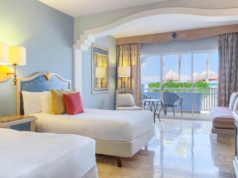 Camera d'hotel luminosa con due letti, lampade moderne e balcone con vista.