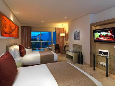 Camera d'hotel moderna con due letti, balcone e TV a parete.