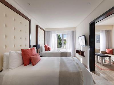 Camera d'hotel luminosa con due letti, testiera imbottita e TV a parete.