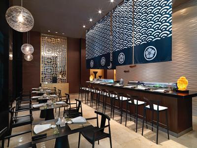 Moderní restaurace s barem, dřevěnými stoly, židlemi a dekorativním osvětlením na stěnách.