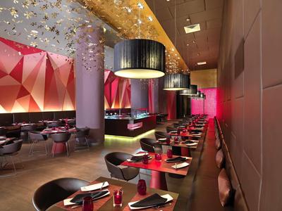 Ristorante moderno con sedie nere, tavoli rossi e illuminazione decorativa.