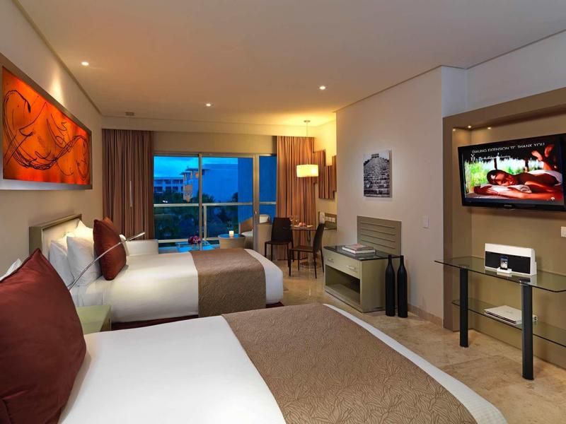 Camera d'hotel moderna con due letti, balcone e TV a parete.