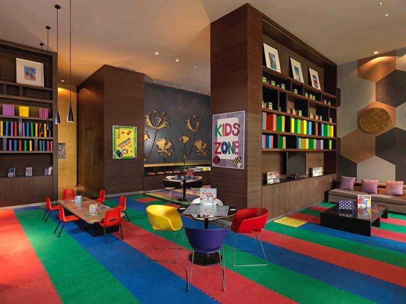 Area giochi colorata per bambini con moquette, sedie colorate e scaffali in uno spazio interno moderno.