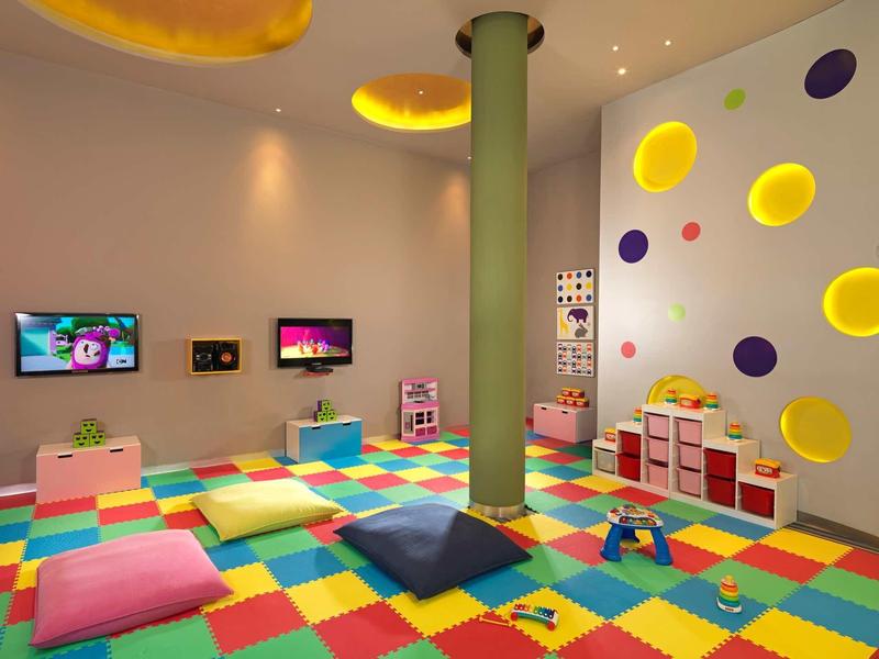Sala giochi colorata per bambini con tappetini, cuscini e parete con accenti rotondi gialli e viola.