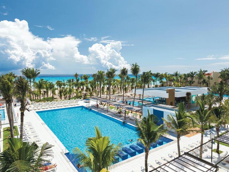 Large outdoor pool with palm trees and a view of the beach on a sunny day.