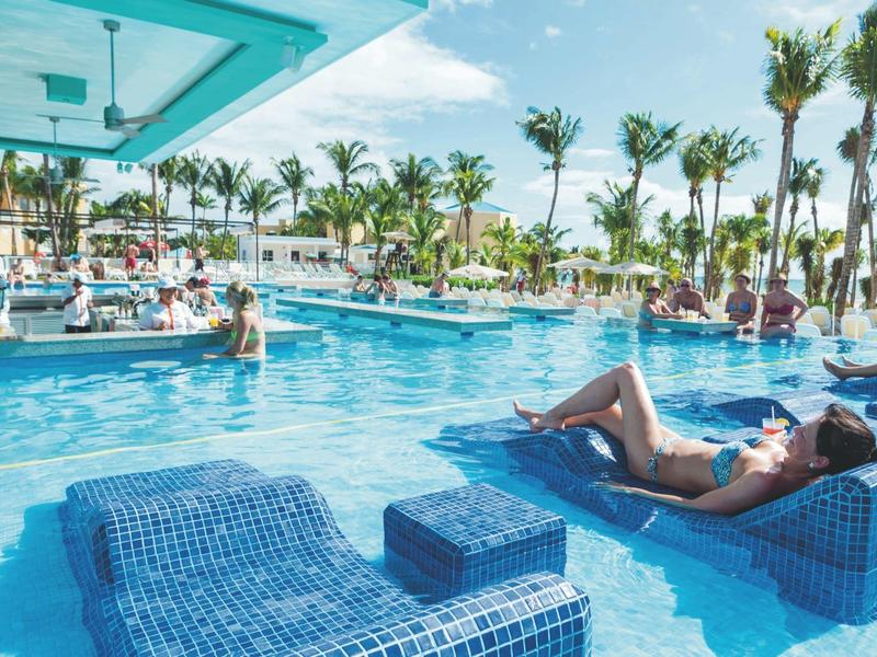 Relaxing person lying by a pool with palm trees and sunshine at a hotel resort.