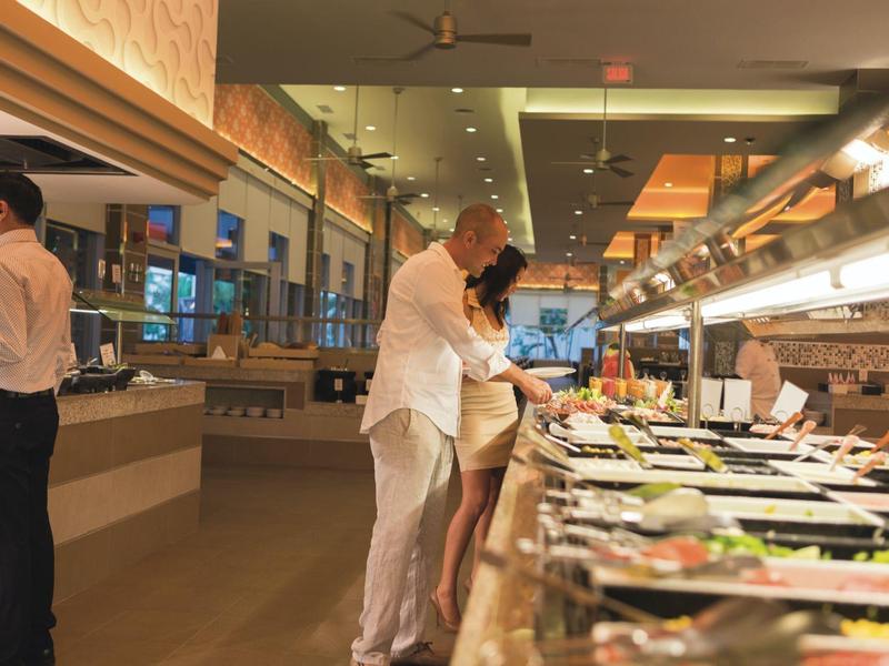Hotel buffet with several guests serving themselves from a long food selection.