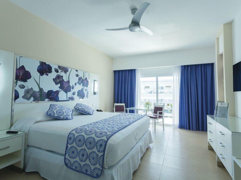 Modern hotel room with double bed, blue accents, and balcony with sea view.