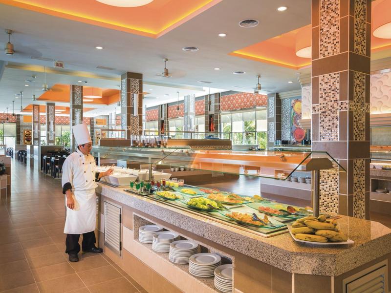 A chef stands by a well-lit buffet display with warm lighting and modern columns.