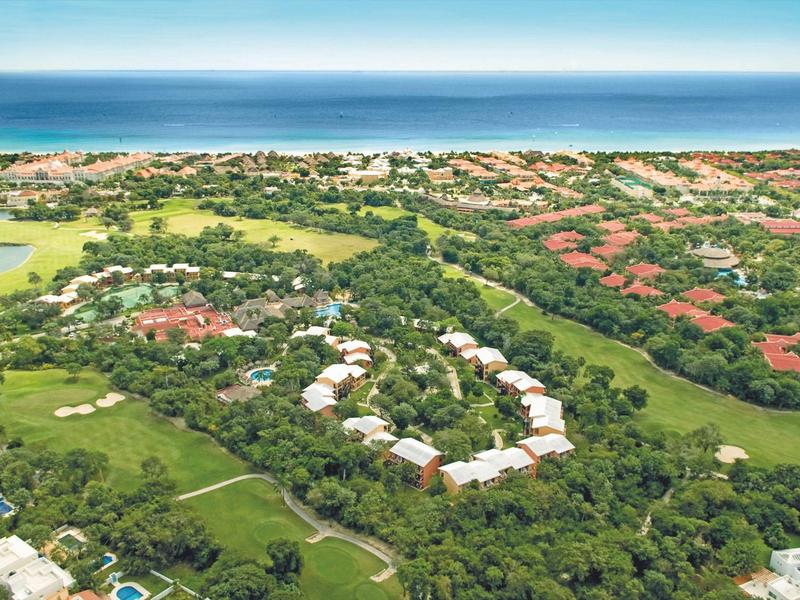 Veduta aerea di un resort costiero con campo da golf verde, edifici e mare sullo sfondo.