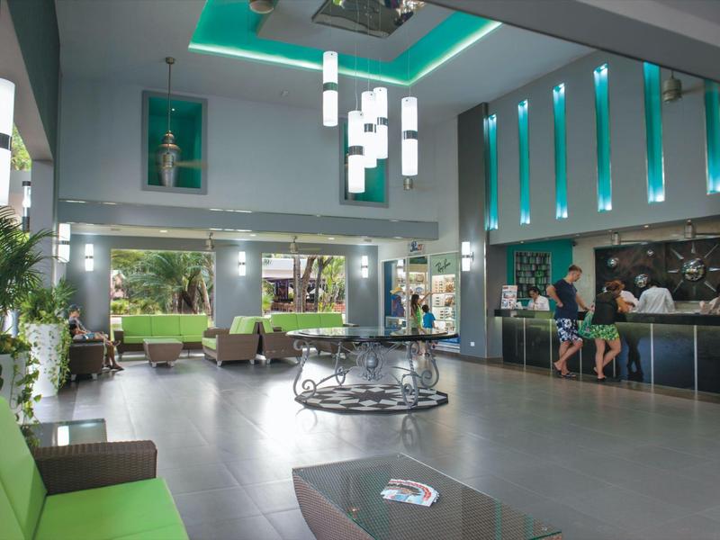 Moderna hall dell'hotel con aree salotto, bar e illuminazione verde accentuata.