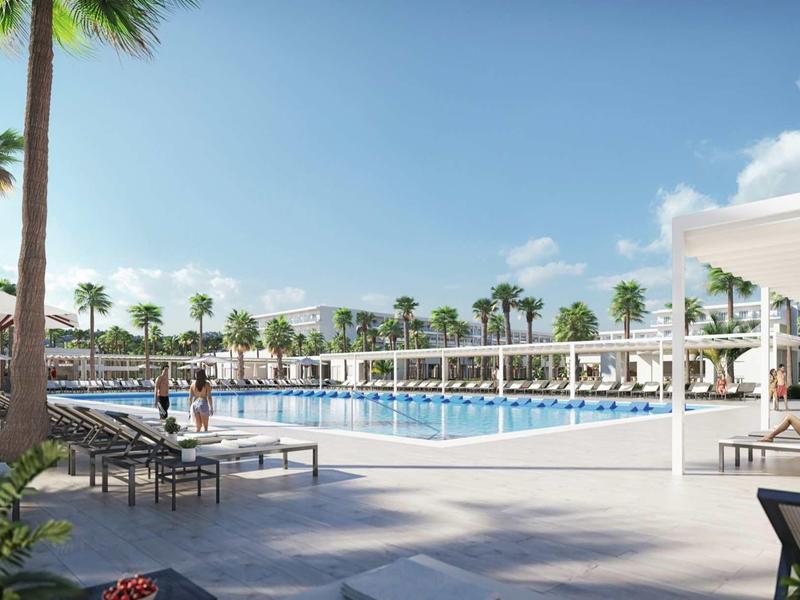 Großer, klarer Pool mit Liegen, Palmen und blauen Himmel in einem modernen Resort.