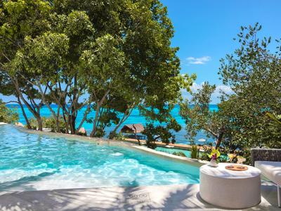 Piscina con vista sul mare, circondata da alberi e zona relax.