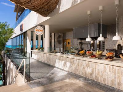 Area buffet aperta con lampade e cibo vicino a un hotel con vista mare.