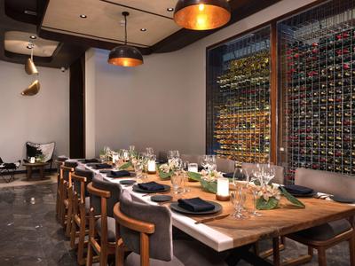 Sala da pranzo elegante con lungo tavolo in legno, parete di vini e posti apparecchiati con stile.