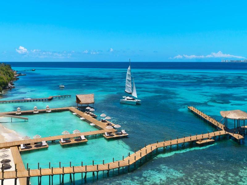 Mare turchese con moli, barca a vela e hotel tropicale fronte mare.