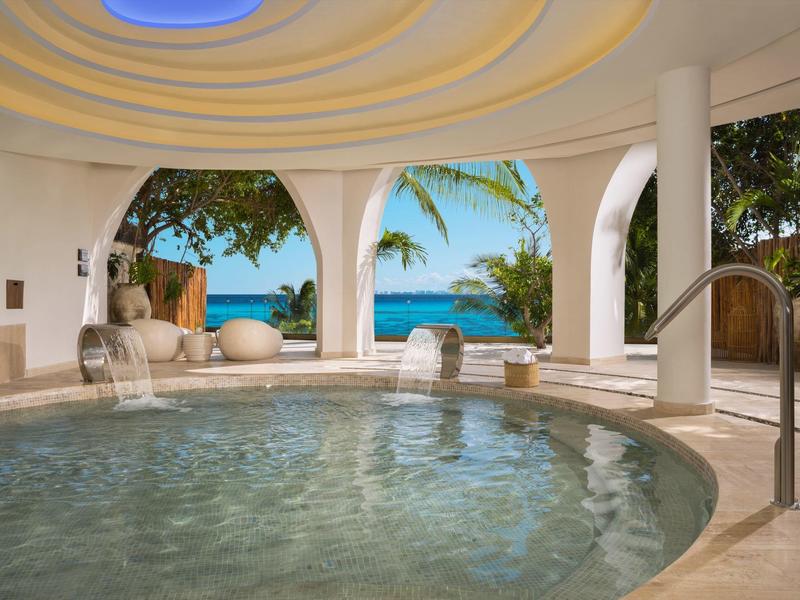 Piscina tonda interna con vista sull'oceano e palme attraverso grandi archi sotto una volta a cupola.