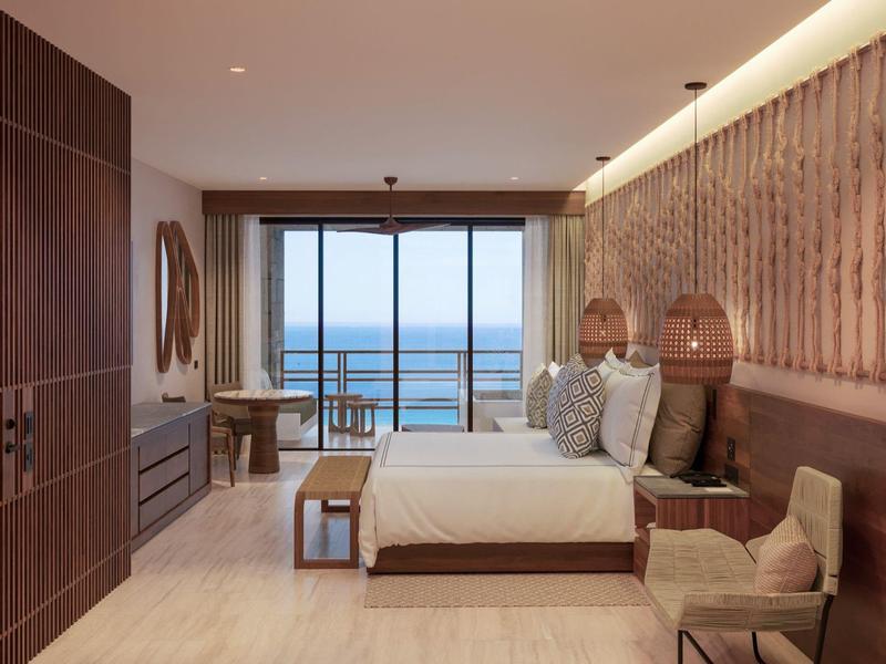 Moderne hotelkamer met tweepersoonsbed, balkon met uitzicht op zee en elegante inrichting in warme tinten.