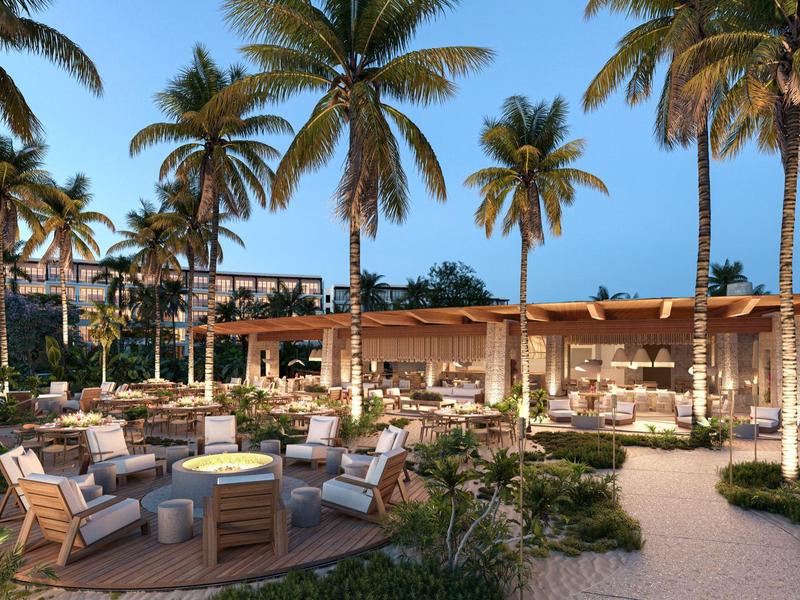 Gezellige buitenruimte van een hotel met zithoeken en palmbomen bij zonsondergang.