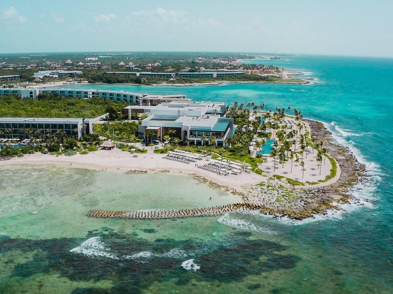 Küstenresort mit Sandstrand, Palmen und klarem Meerwasser an einer felsigen Halbinsel.