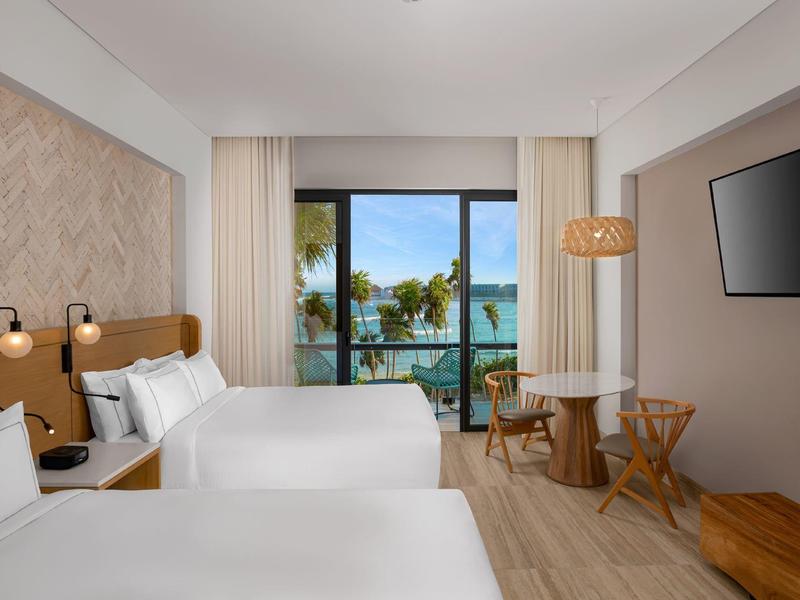 Hell eingerichtetes Hotelzimmer mit zwei Betten, Blick auf Terrasse, Holzmöbeln und Wand-TV.