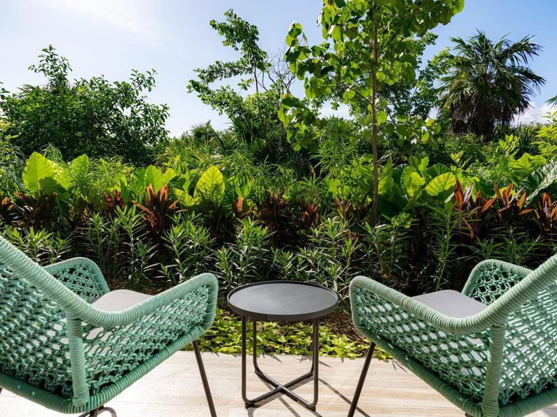 Zwei grüne Stühle und ein runder Tisch stehen auf einer Terrasse vor dichter grüner Pflanzenwand.