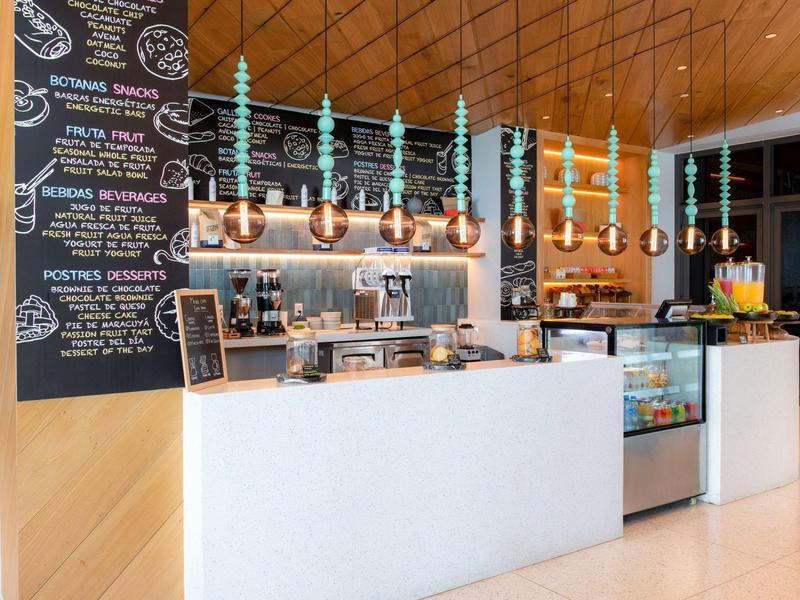 Kaffeetheke mit hellen Holzdecken, Hängelampen, Kaffeemaschinen und großer Tafel mit Angeboten.