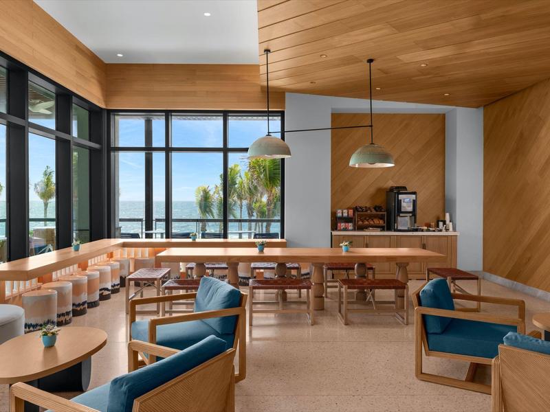 Moderner Caféraum mit Holzmöbeln, blauen Sesseln, großen Fenstern und Blick aufs Wasser.