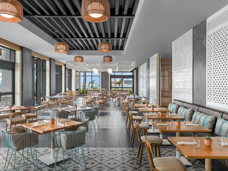 Modernes Restaurant mit Holz- und Metallstühlen, Holztischen und großen Fenstern für viel Tageslicht.