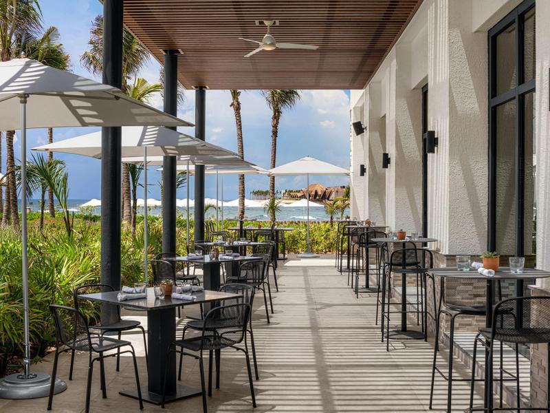 Terrassenbereich eines Restaurants mit schwarzen Metallstühlen, Tischen und Sonnenschirmen am Meer.