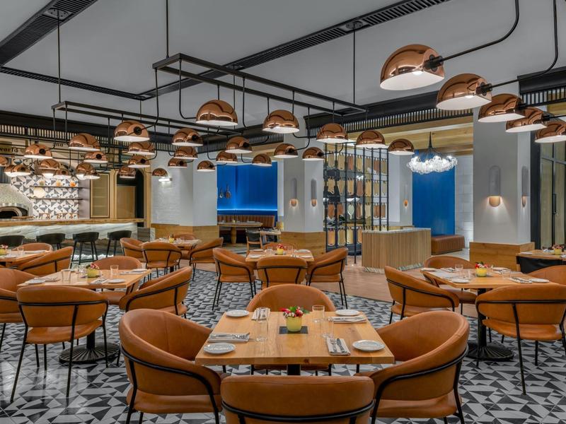 Modernes Restaurant mit braunen Ledersesseln, hängenden Kupferlampen und geometrischem Bodenmuster.